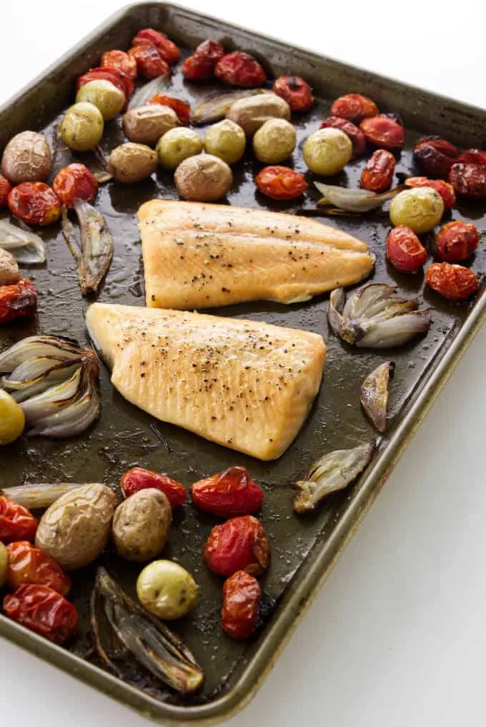 Two fillets of baked arctic char on a sheet pan with vegetables.