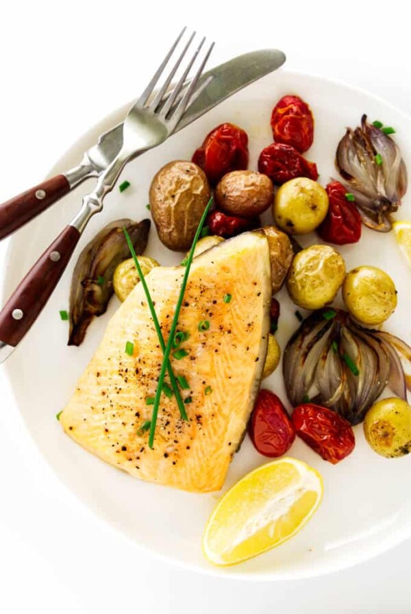 Baked arctic char with vegetables on a plate with a fork and knife.