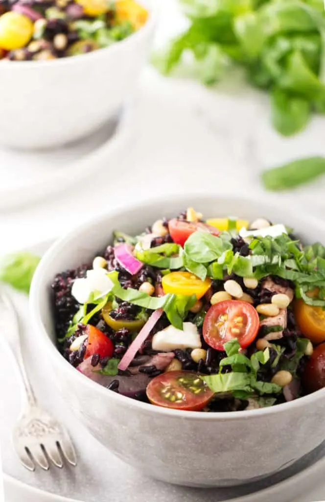 A bowl of black rice salad with tomatoes and basil.