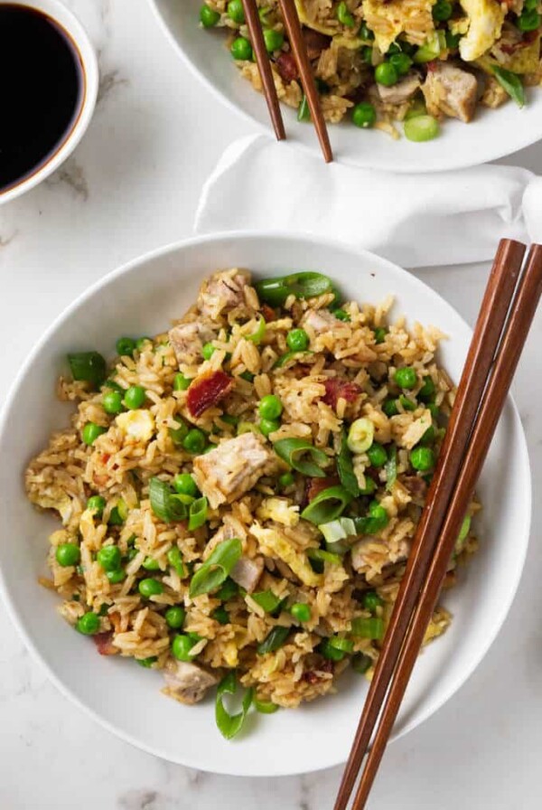 Two bowls of pork fried rice with chopsticks.