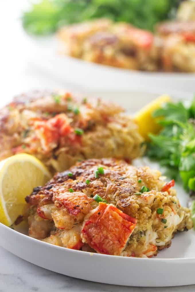 Alaskan King crab cakes on a plate with lemon slices and salad greens.