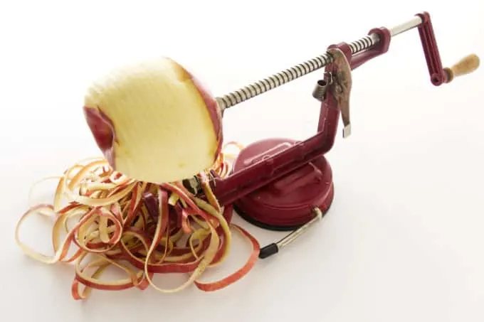 An apple on a apple-peeler with apple peels on the counter.