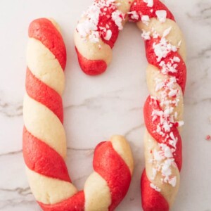 Two candy cane cookies on a white marble background.