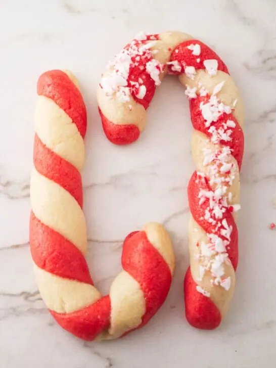 Two candy cane cookies on a white marble background.