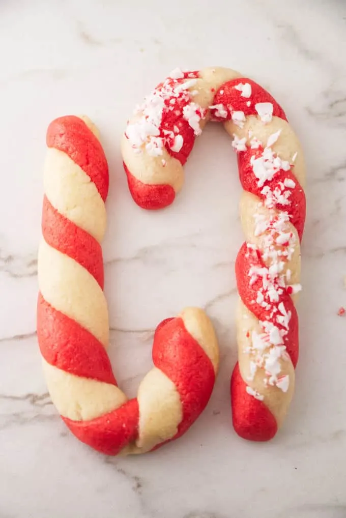 Two candy cane cookies on a white marble background.