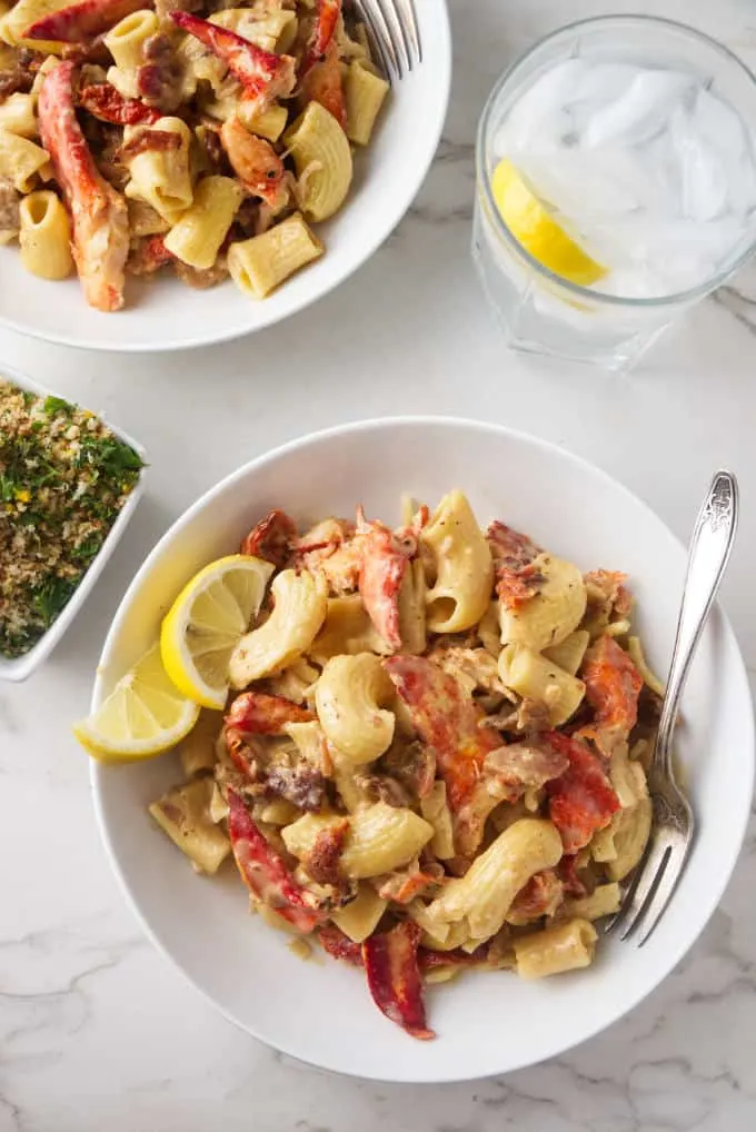 Overhead photo of 2 bowls with lobster pasta, a glass of water and crispy panko bread crumbs with lemon and garlic.