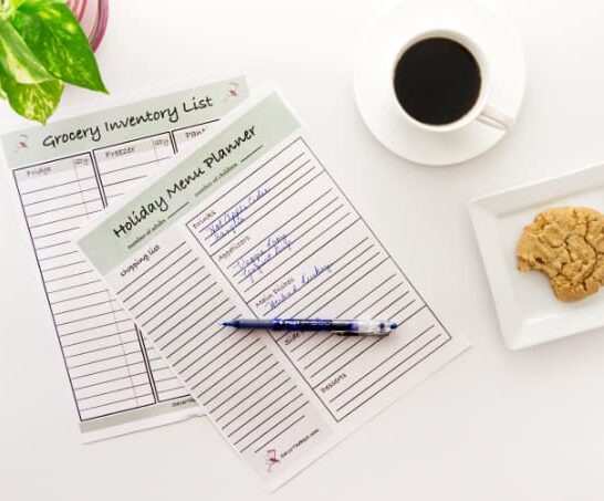 A holiday menu planner on a desk with coffee and a cookie and a pen.