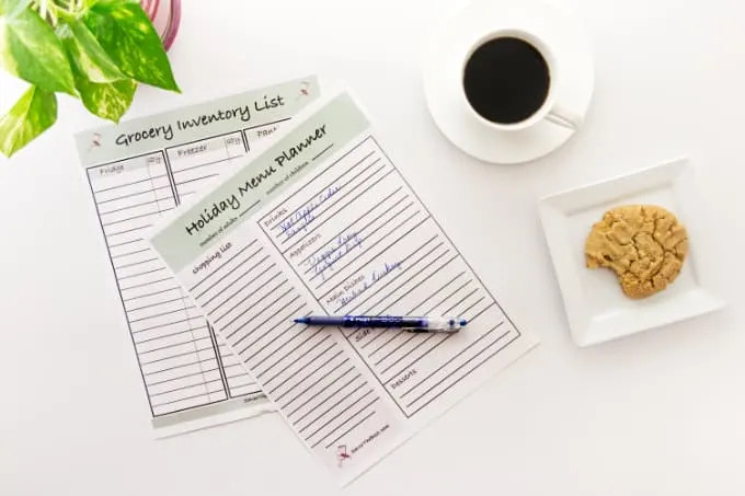 A holiday menu planner on a desk with coffee and a cookie and a pen.