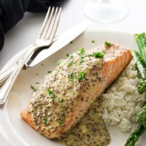 A King salmon fillet with mustard sauce on a plate with rice and asparagus.