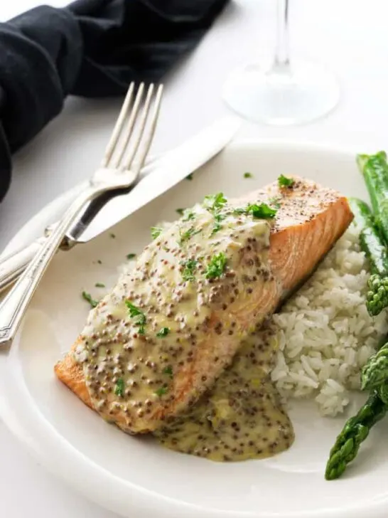 A King salmon fillet with mustard sauce on a plate with rice and asparagus.
