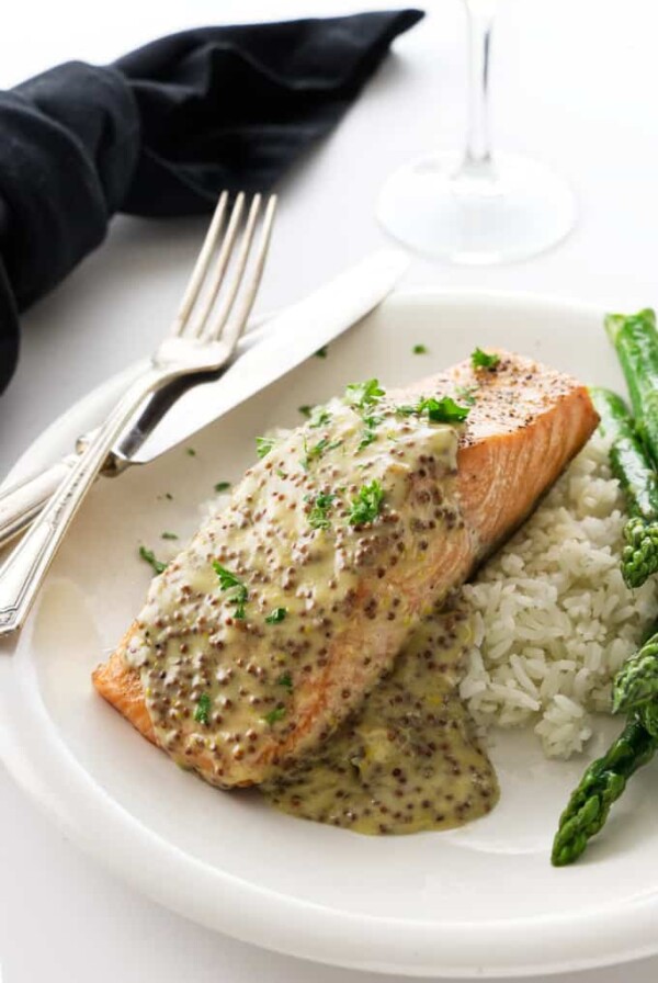 A King salmon fillet with mustard sauce on a plate with rice and asparagus.