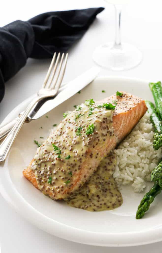 A King salmon fillet with mustard sauce on a plate with rice and asparagus.