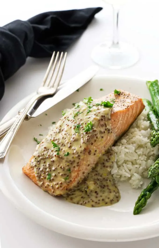 A King salmon fillet with mustard sauce on a plate with rice and asparagus.