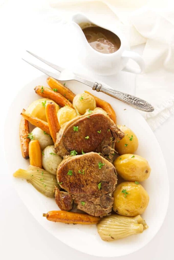 Two pork chops and veggies on a serving platter with a dish of gravy on the side.