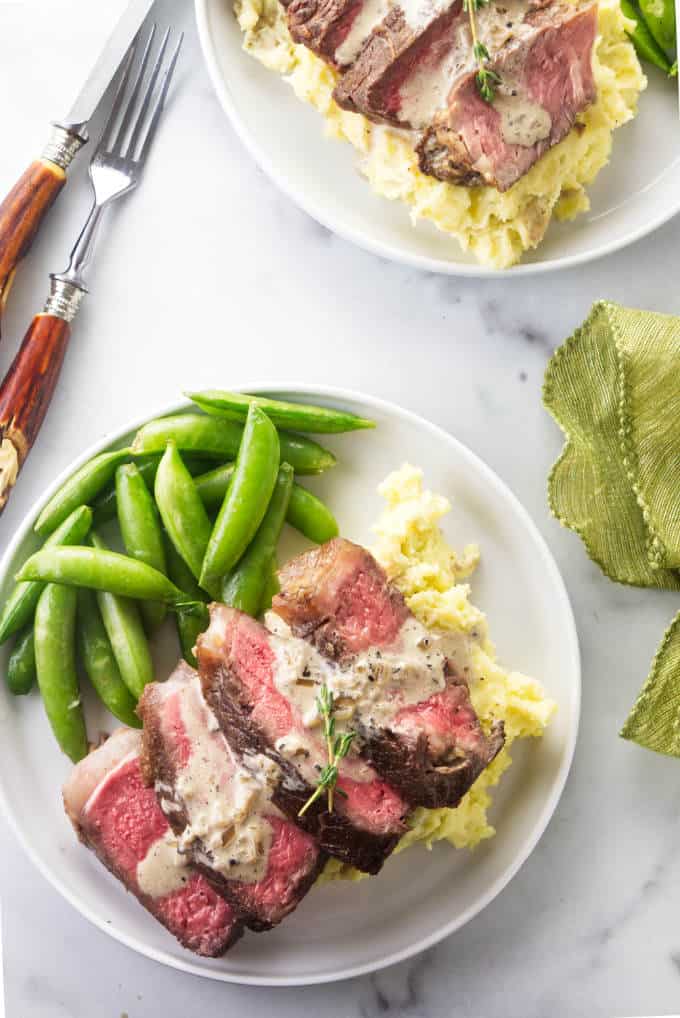 Two plates of bison ribeye steak with mashed potatoes and snap peas.