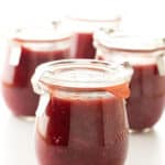 A jar of strawberry fig jam with fresh strawberries and figs in the background.