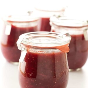 A jar of strawberry fig jam with fresh strawberries and figs in the background.