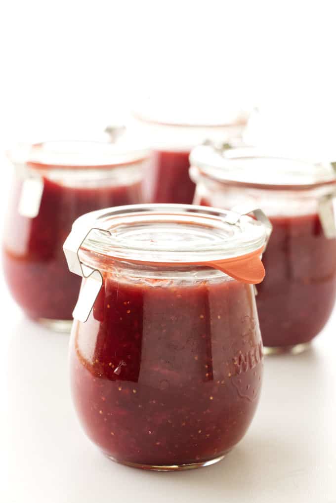 A jar of strawberry fig jam with fresh strawberries and figs in the background.