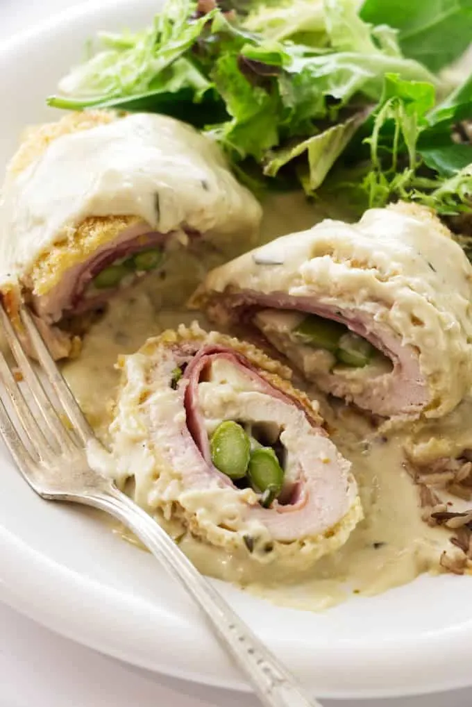A plate of chicken cordon bleu with asparagus on a plate with salad.