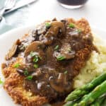 A close up of Jaeger Schnitzel and mushroom sauce on a plate with asparagus.