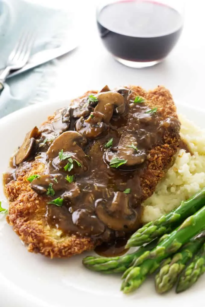 A close up of Jaeger Schnitzel and mushroom sauce on a plate with asparagus.