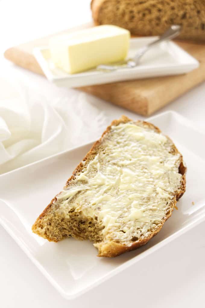 A buttered slice of rye bread with a butter dish in the background.