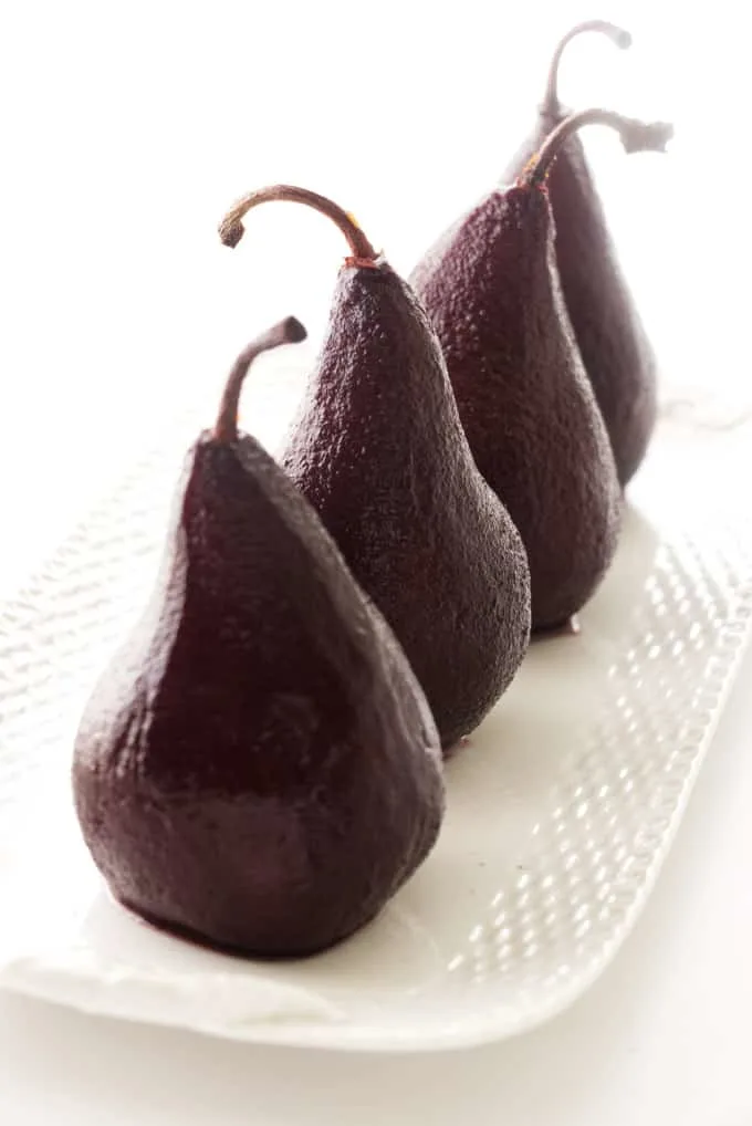 Four red wine poached pears on a serving platter.