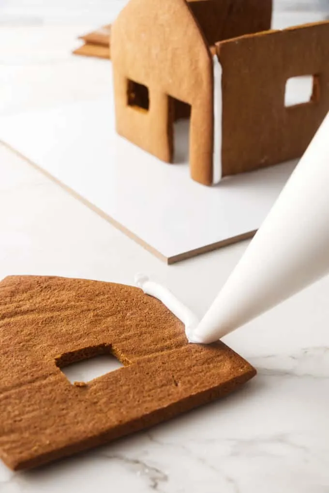 Piping icing on the front of a gingerbread house.