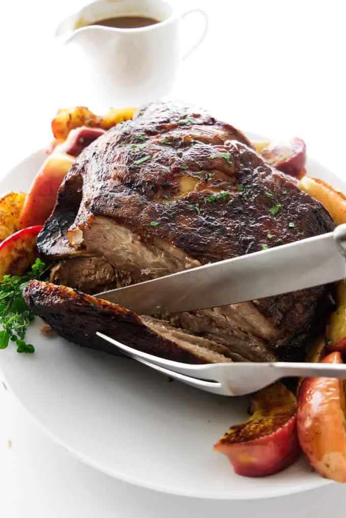 A serving of pork roast being sliced and apples next to the roast.