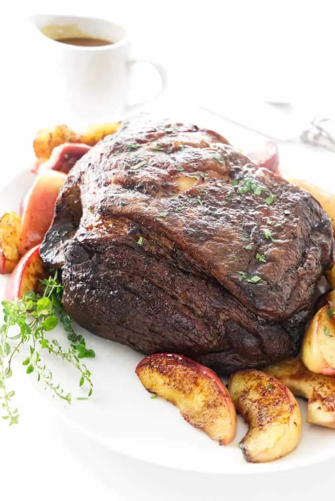 A roasted pork roast with apples on a platter and gravy in the background.