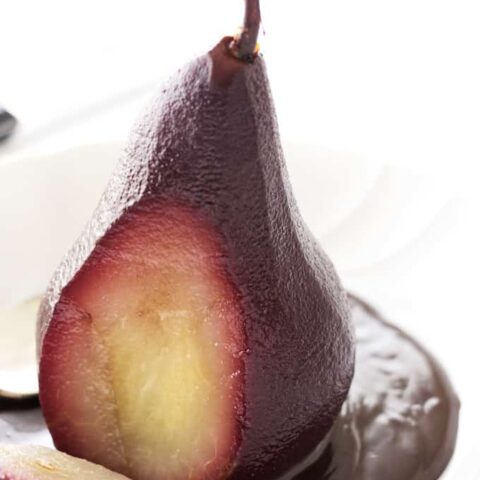 A red wine poached pear with a slice through it to show the contrasting fruit on the inside.