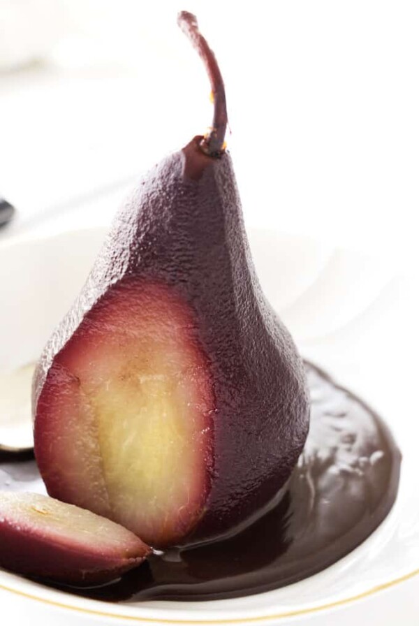 A red wine poached pear with a slice through it to show the contrasting fruit on the inside.