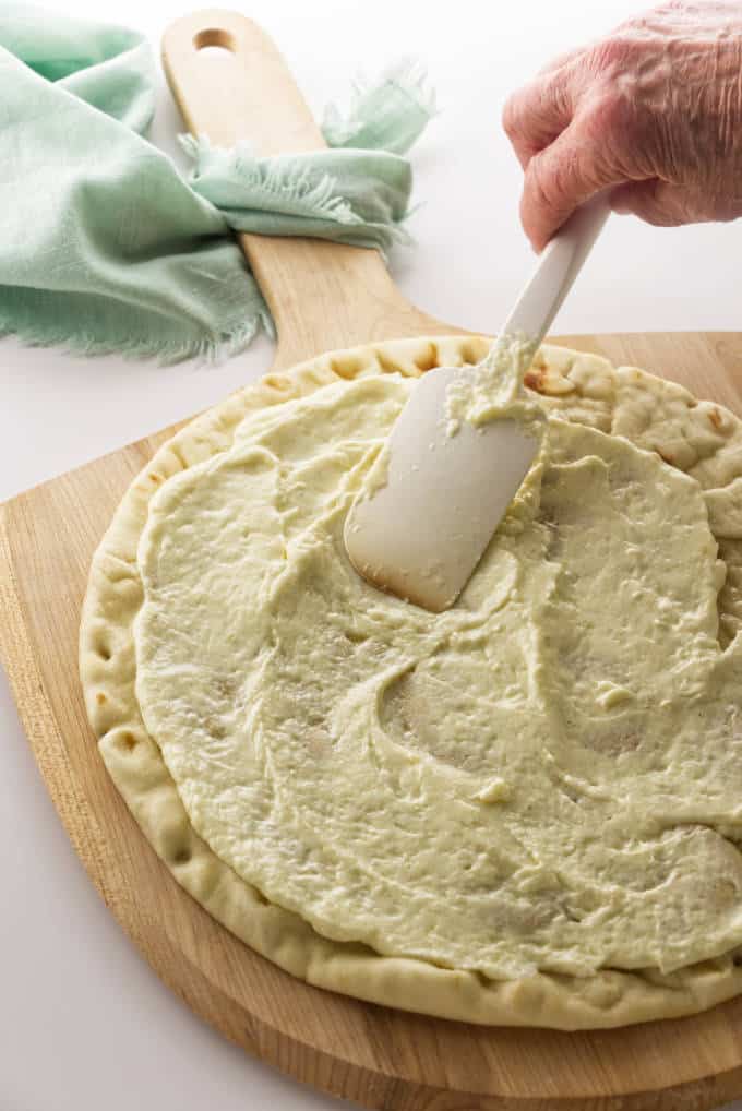 White garlic sauce being spread on a pizza crust.