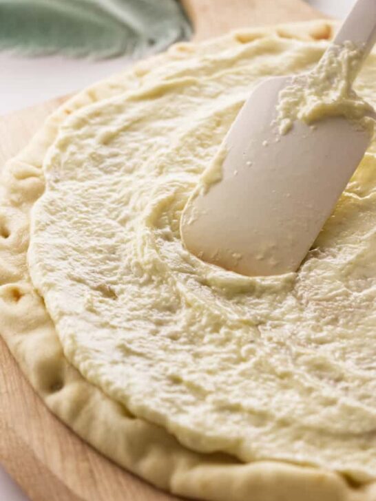 A pizza crust with white garlic sauce.