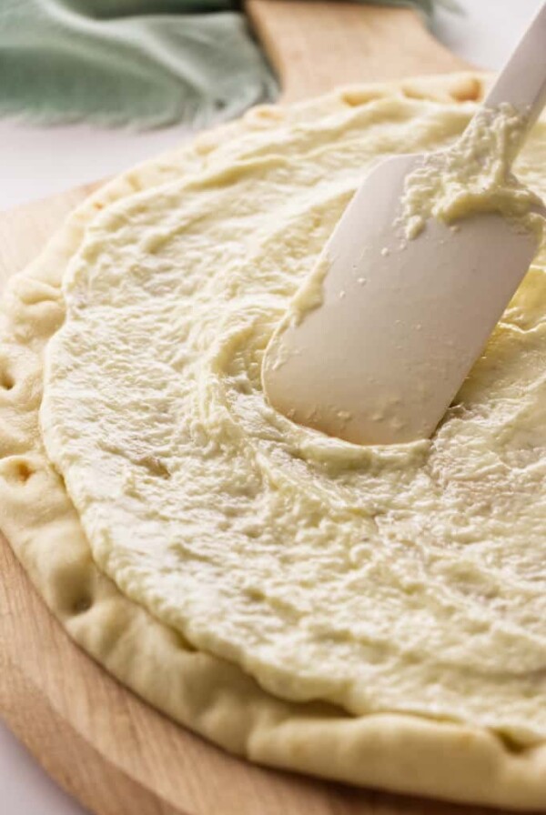 A pizza crust with white garlic sauce.