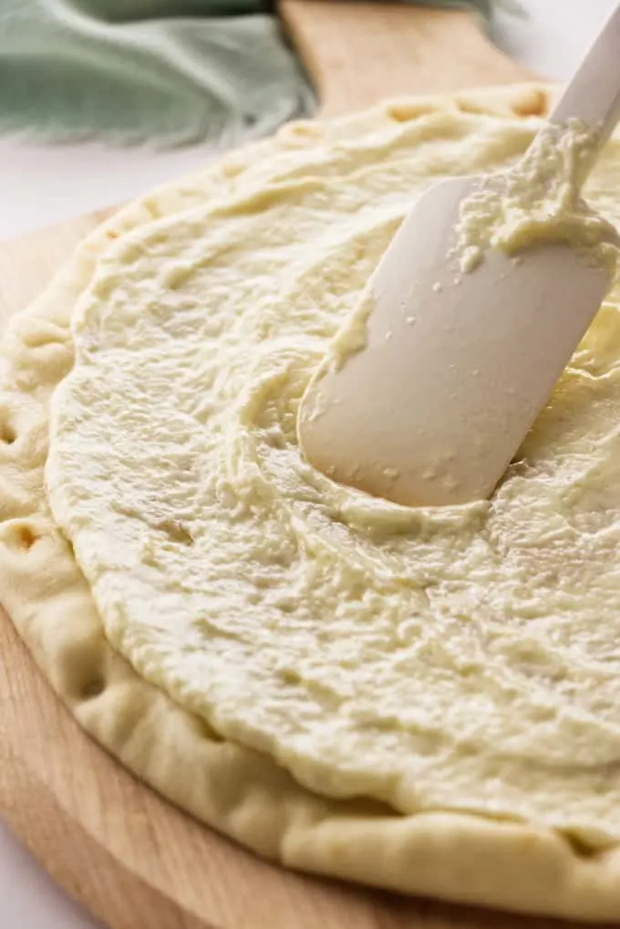 A pizza crust with white garlic sauce.