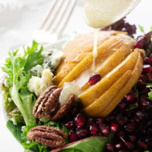 Dijon lemon vinaigrette being drizzled on pomegranate pear salad.