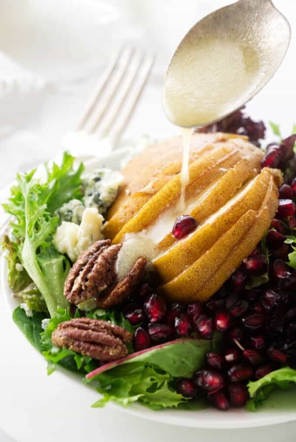 Dijon lemon vinaigrette being drizzled on pomegranate pear salad.