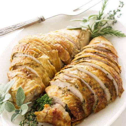 A sliced turkey breast on a serving platter with herbs.