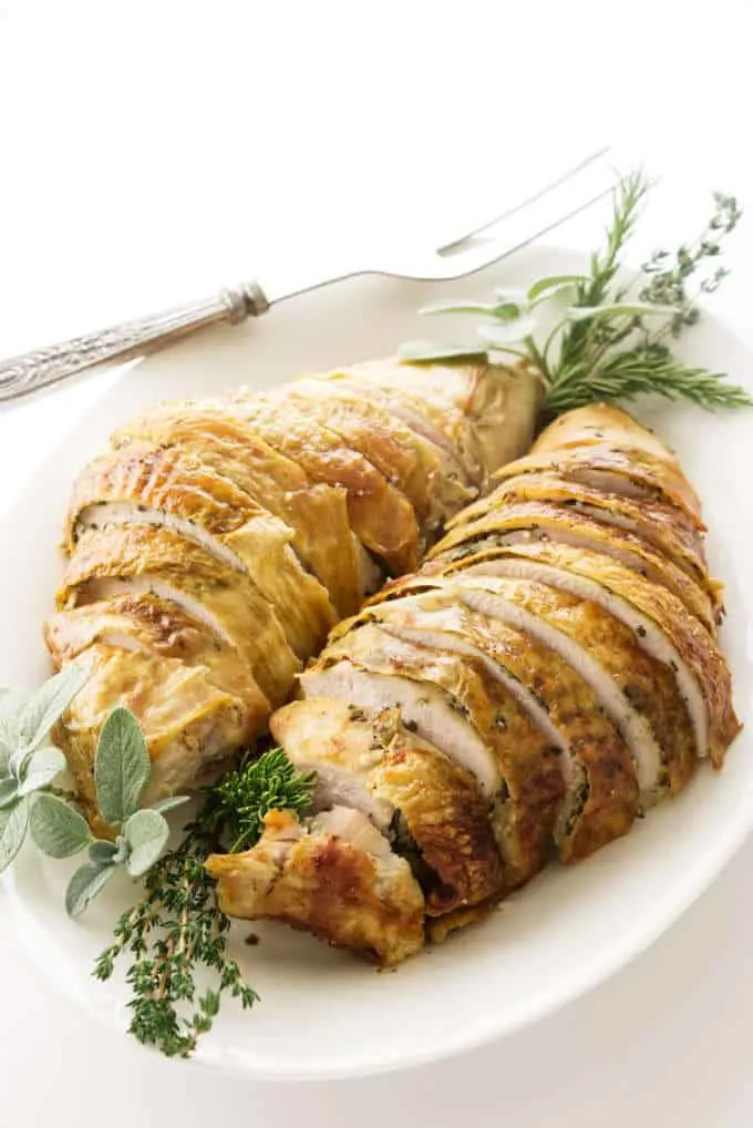 A sliced turkey breast on a serving platter with herbs.