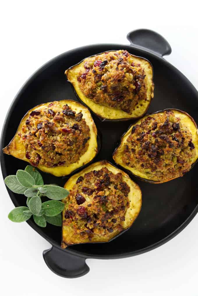 Four halves of acorn squash stuffed with sausage dressing and placed on a black serving plate.