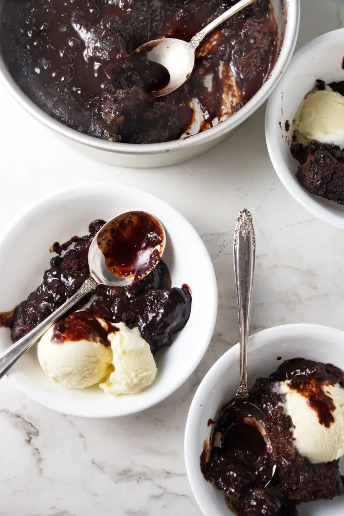 A cake pan and three bowls with hot fudge cake and ice cream.