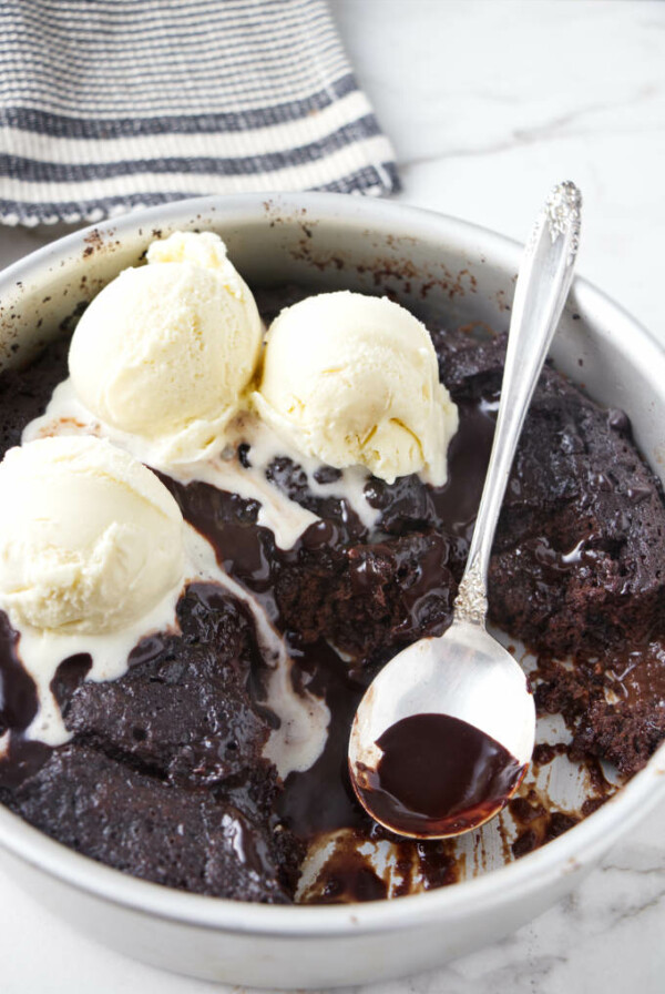 A cake pan with hot fudge cake topped with three scoops of vanilla ice cream.