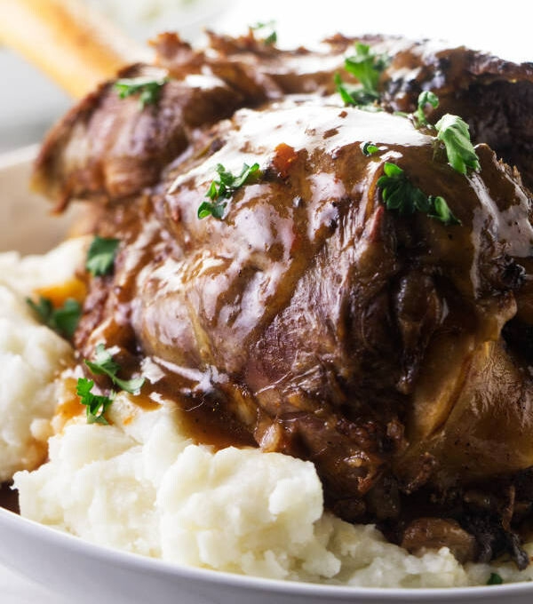 A lamb shank on a bed of mashed potatoes with gravy on top.