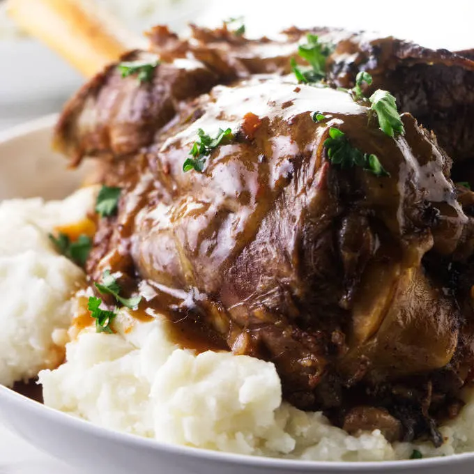 A lamb shank on a bed of mashed potatoes with gravy on top.