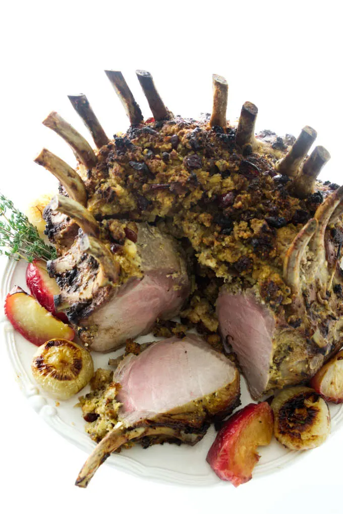 Overhead view of crown pork roast with cut servings, stuffing, apples and onions