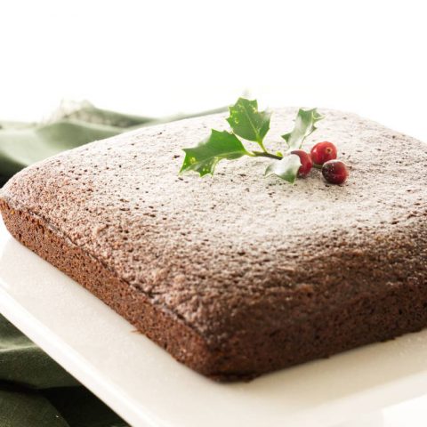 Stout gingerbread cake on pedestal, dusting of sugar 'snow' and holly/berry decorations