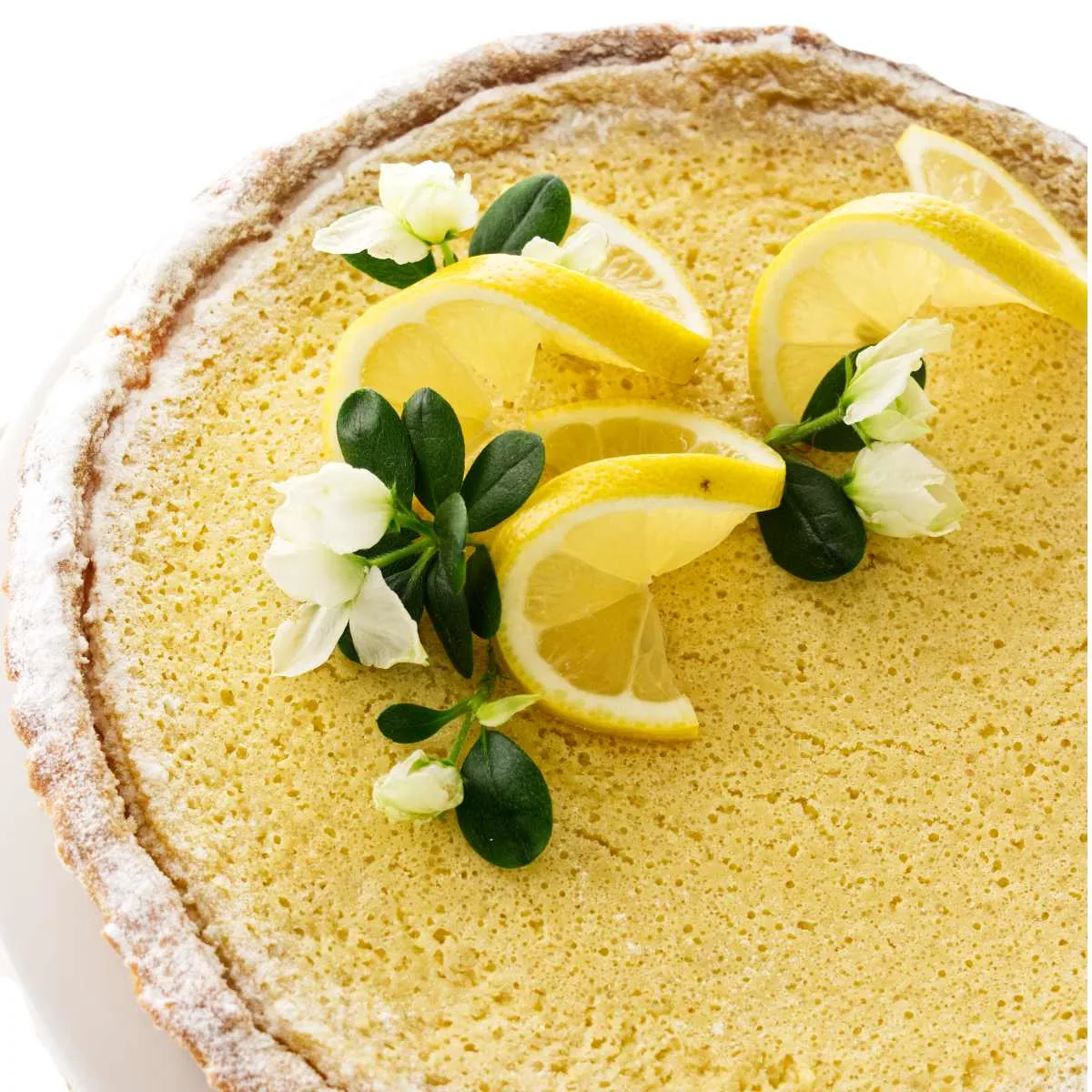 Close up overhead view of creamy whole lemon tart garnished with lemon slices and white blossoms