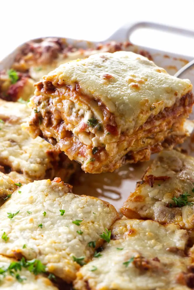 Sausage and beef lasagna being scooped out of a casserole dish.