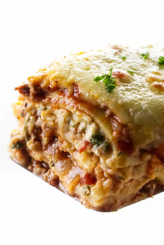 A square slice of lasagna with sausage and beef on a spatula.